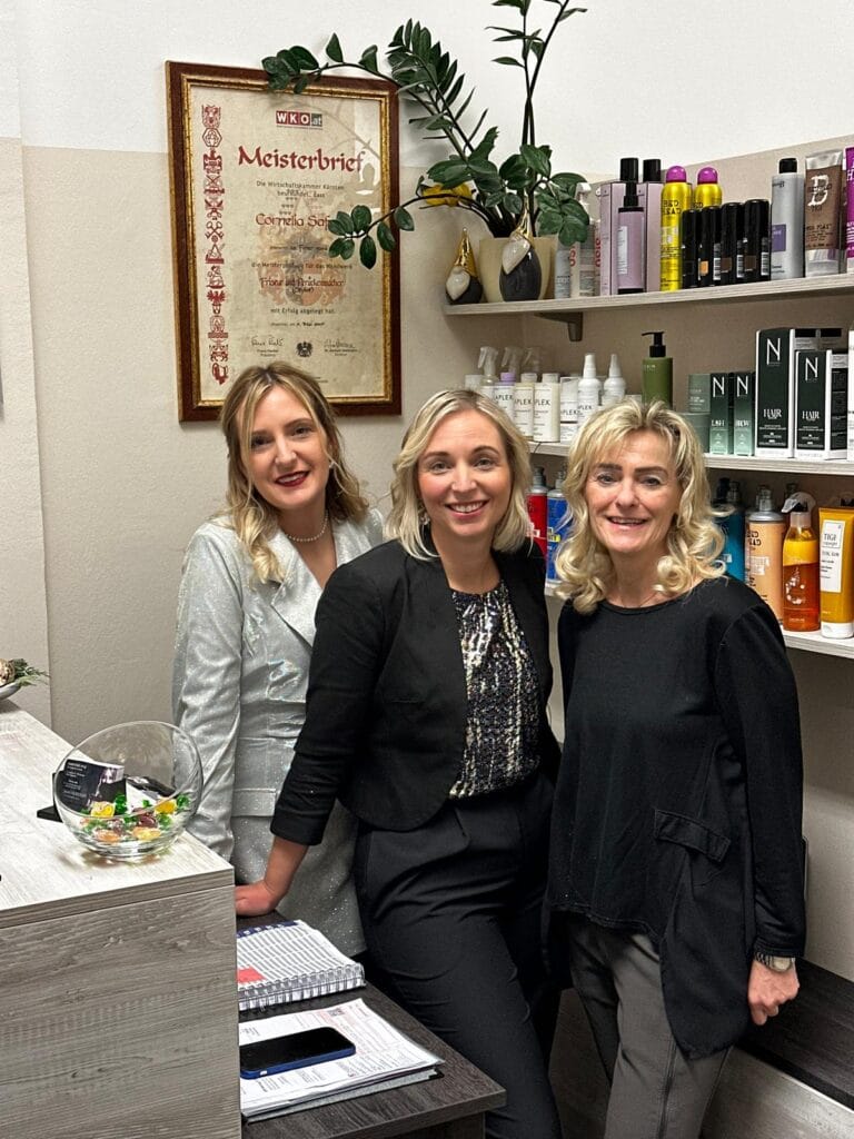 Bild von Haarstudio Style in Klagenfurt, das die Inhaberin Frau Cornelia Buchsbaum mit zwei Mitarbeitenden zeigt. Der Salon bietet eine breite Palette an Friseurdiensten, darunter Haarverlängerungen, Extensions und Haarverdichtung. Das Studio ist bekannt für seine hochwertigen Produkte und Dienstleistungen, die in einem modernen und einladenden Ambiente durchgeführt werden. Im Hintergrund sind Regale mit diversen Haarprodukten und Styling-Tools zu sehen, die die Professionalität und Vielfalt des Angebots unterstreichen. Die Einrichtung spiegelt die Expertise und das Engagement für Qualität und Kundenzufriedenheit wider, was Haarstudio Style zu einem bevorzugten Friseursalon in Klagenfurt macht.